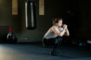 A man is doing squats in a gym with a punching bag. The setting appears stylish and focused on fitness.