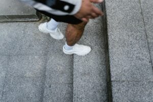 Person wearing white sneakers taking steps on gray stone stairs outdoors.
